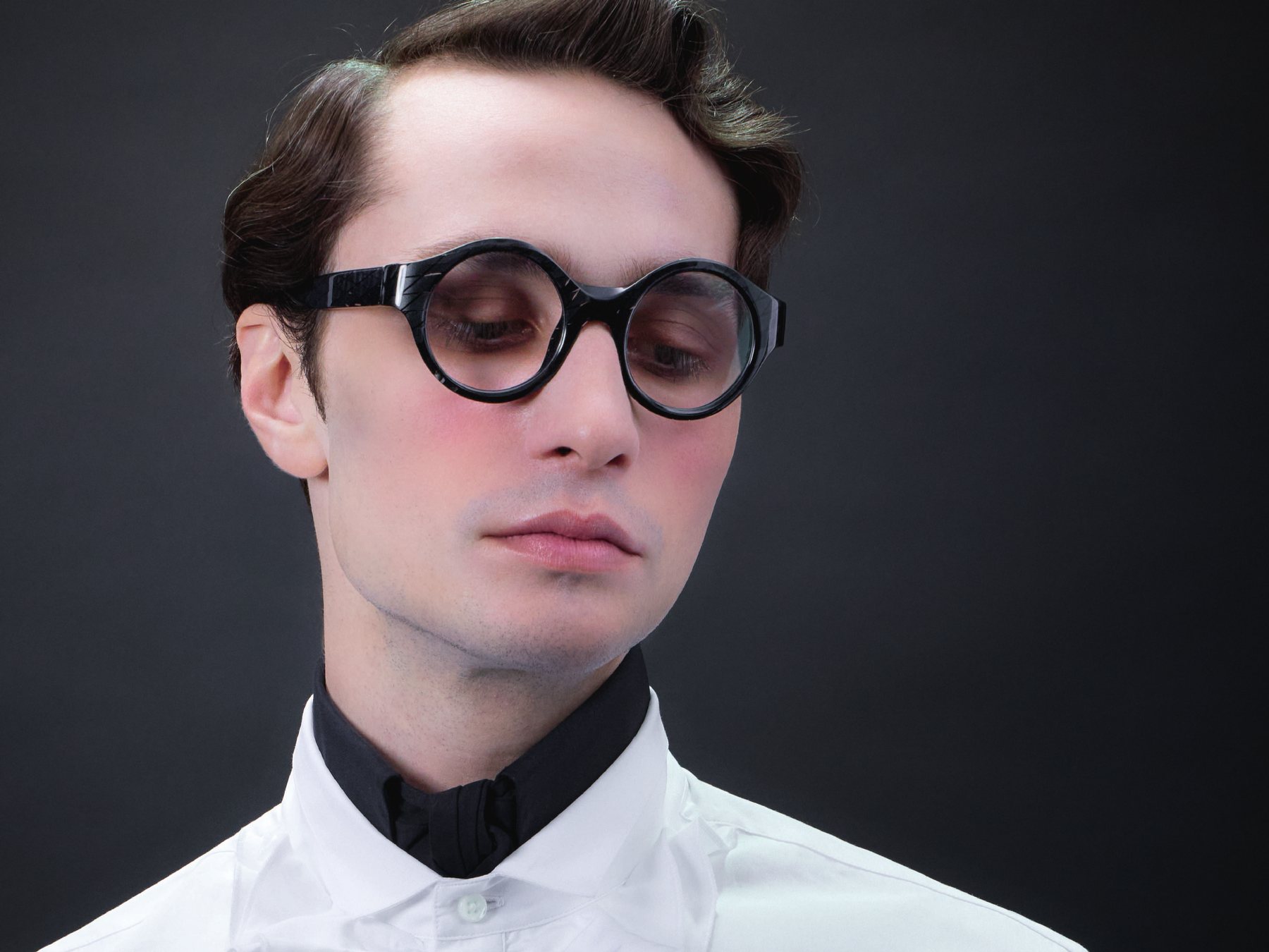 Alain Mikli campaign portrait of a model in a white ruffled shirt wearing round black Alain Mikli frames